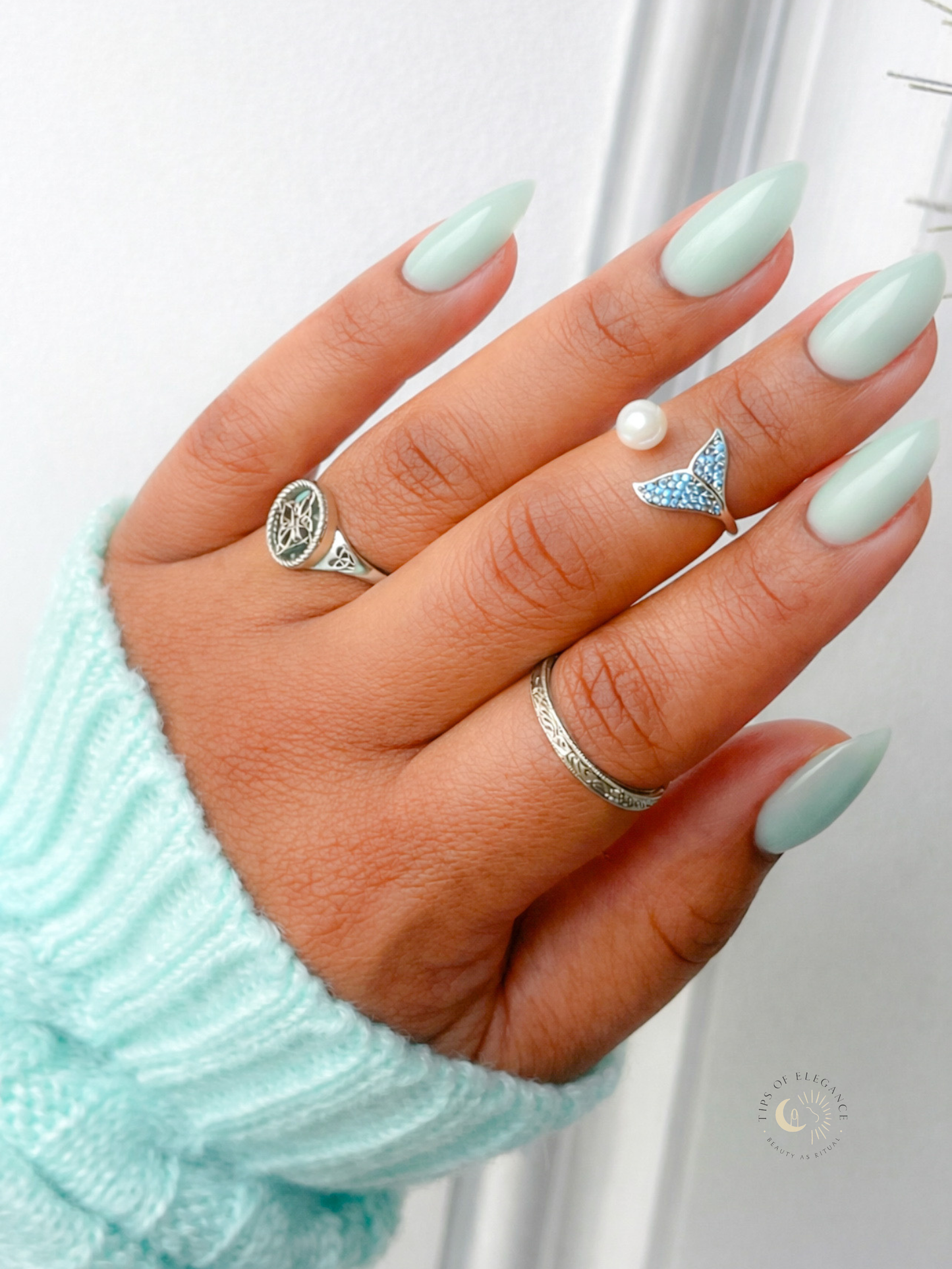 Hand with mint green nail polish wearing two rings on a white background