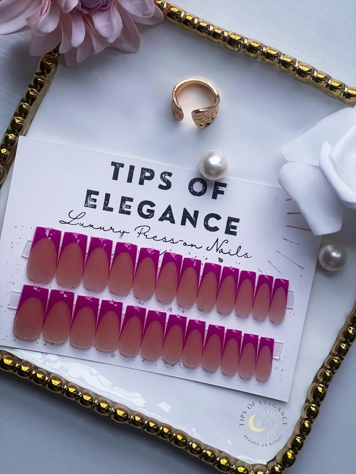 Set of false nails with 'Tips of Elegance' branding, surrounded by a ring and pearls on a decorative tray.