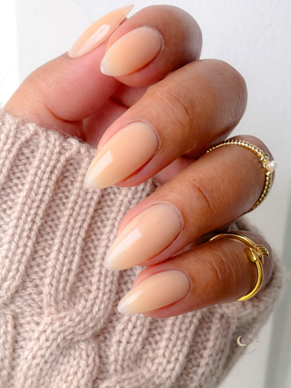 Hand with beige nail polish and gold rings on a neutral background