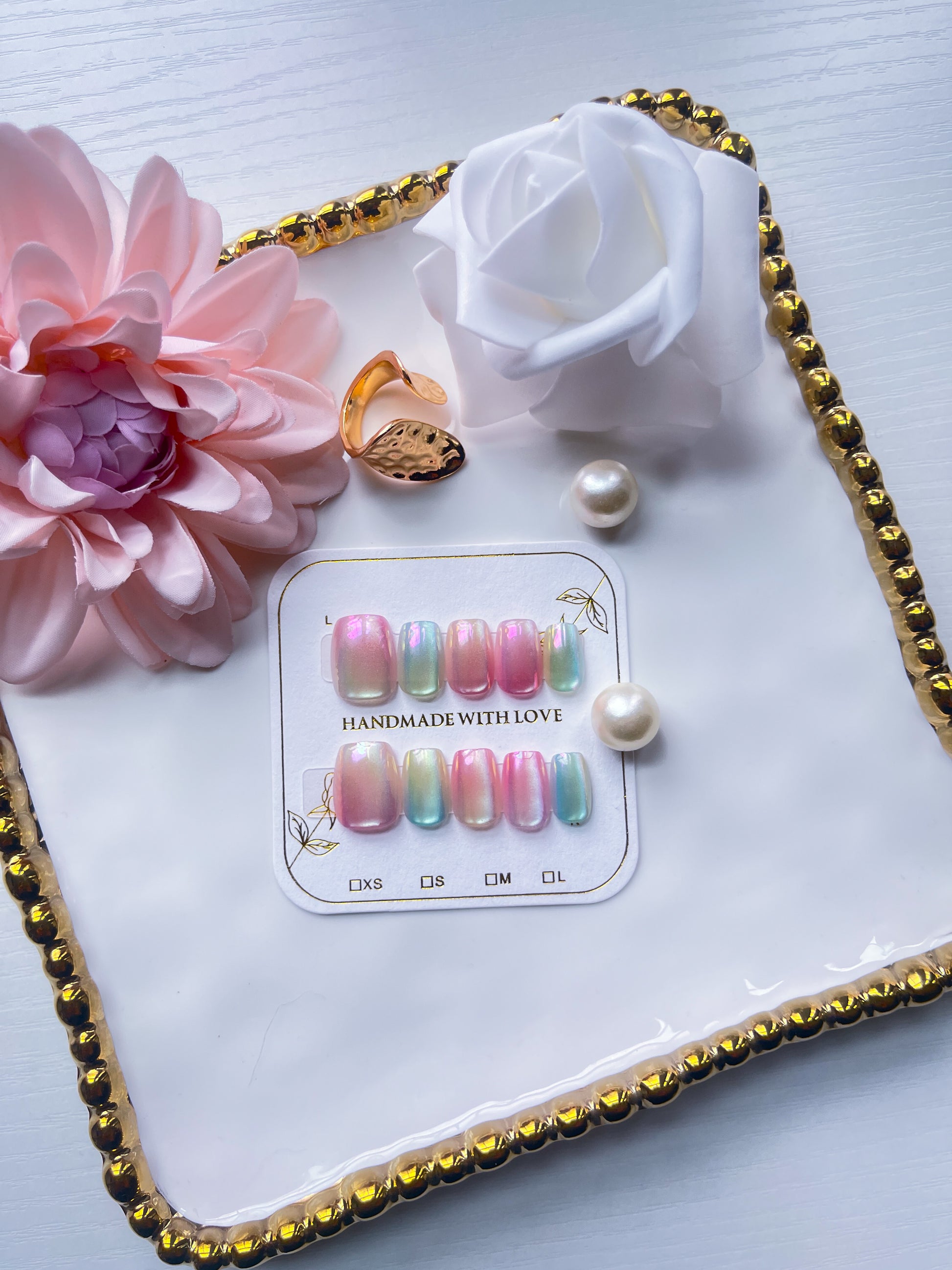 Set of colorful nail art designs on a card with a ring, pearl, and flowers on a decorative tray.