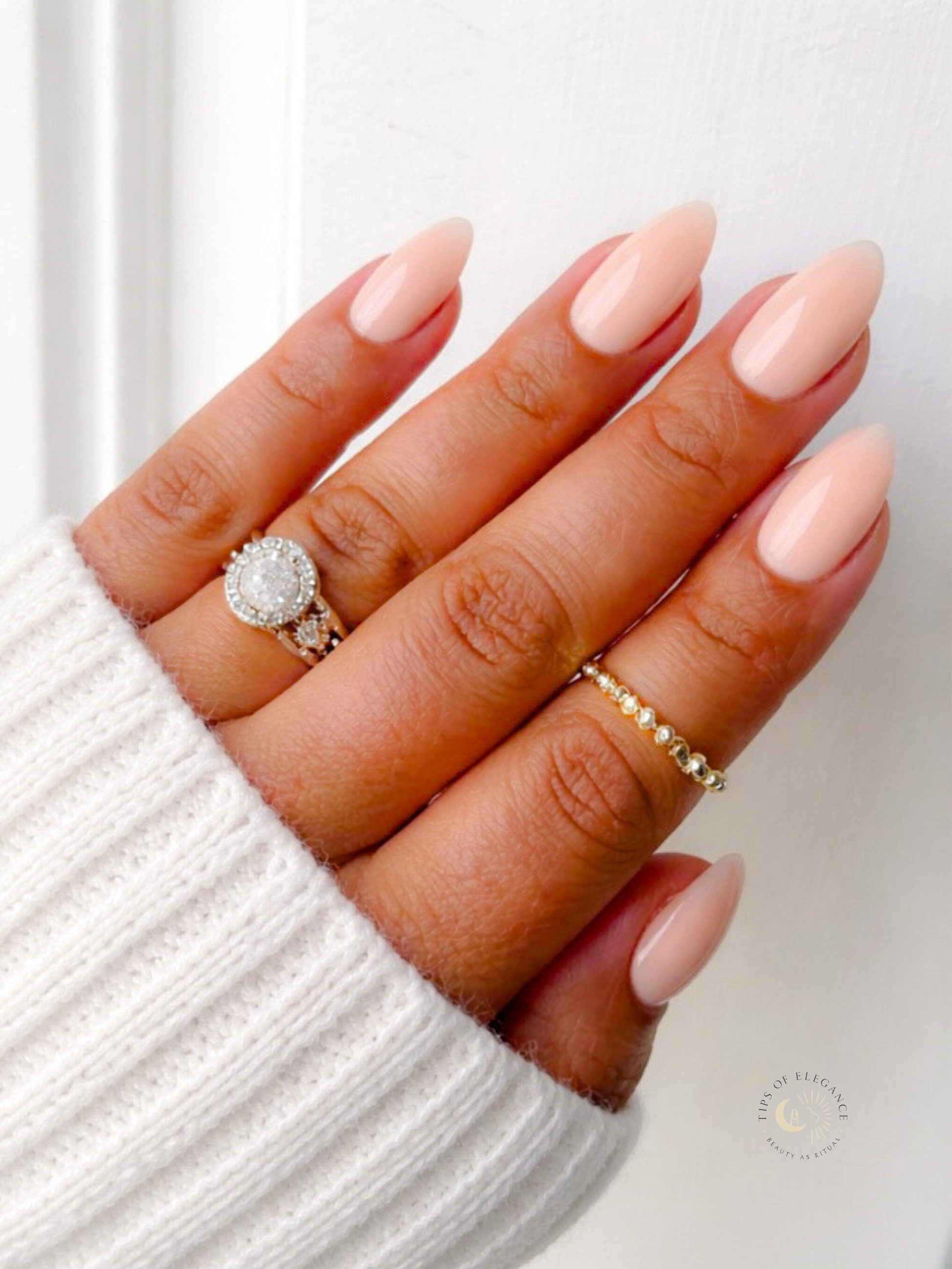 Hand with Peachy nude polish wearing two rings on a white background
