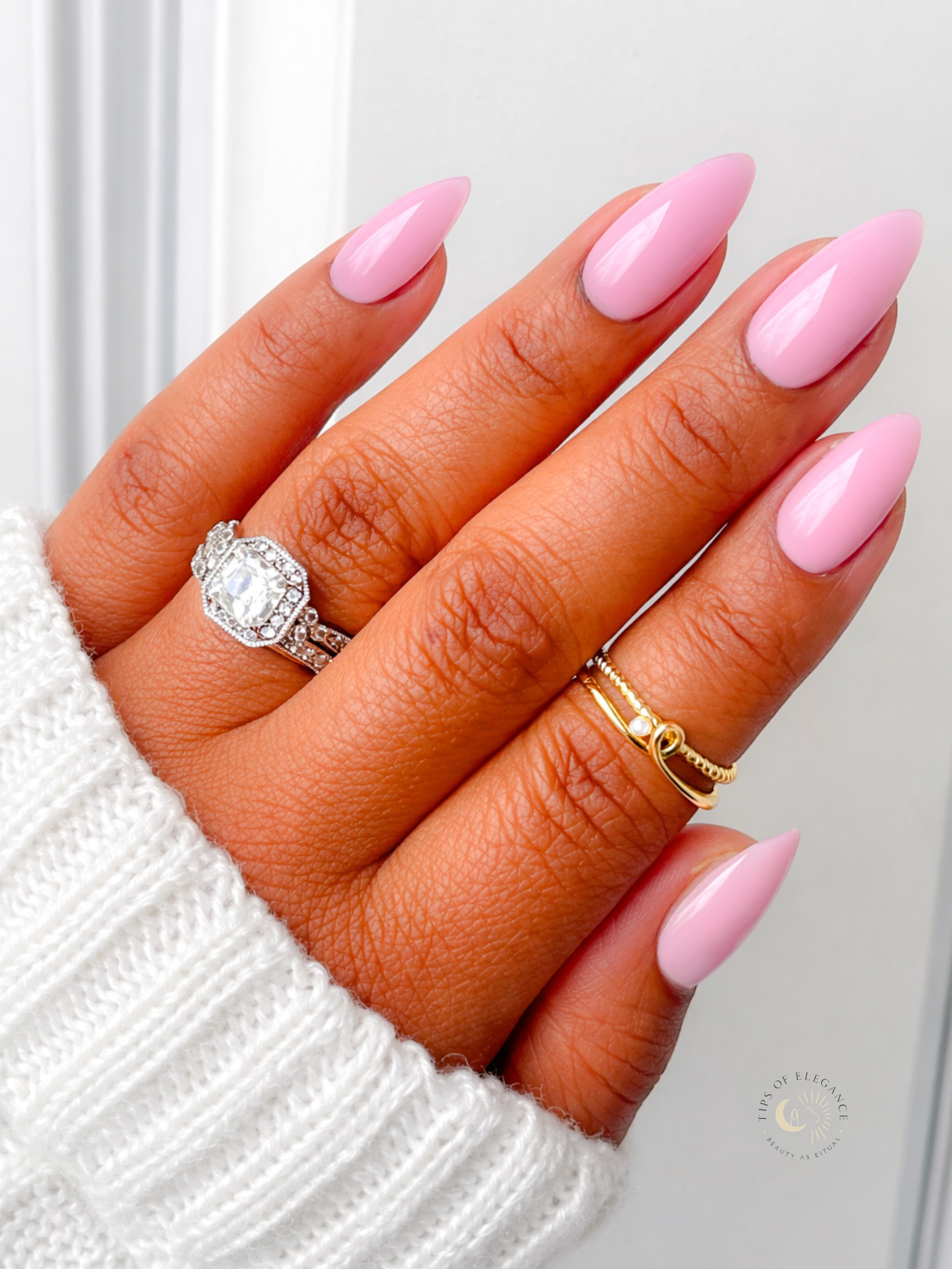 Hand with pink nails wearing two rings on a white background
