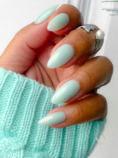 Hand with light green nail polish wearing a turquoise sweater