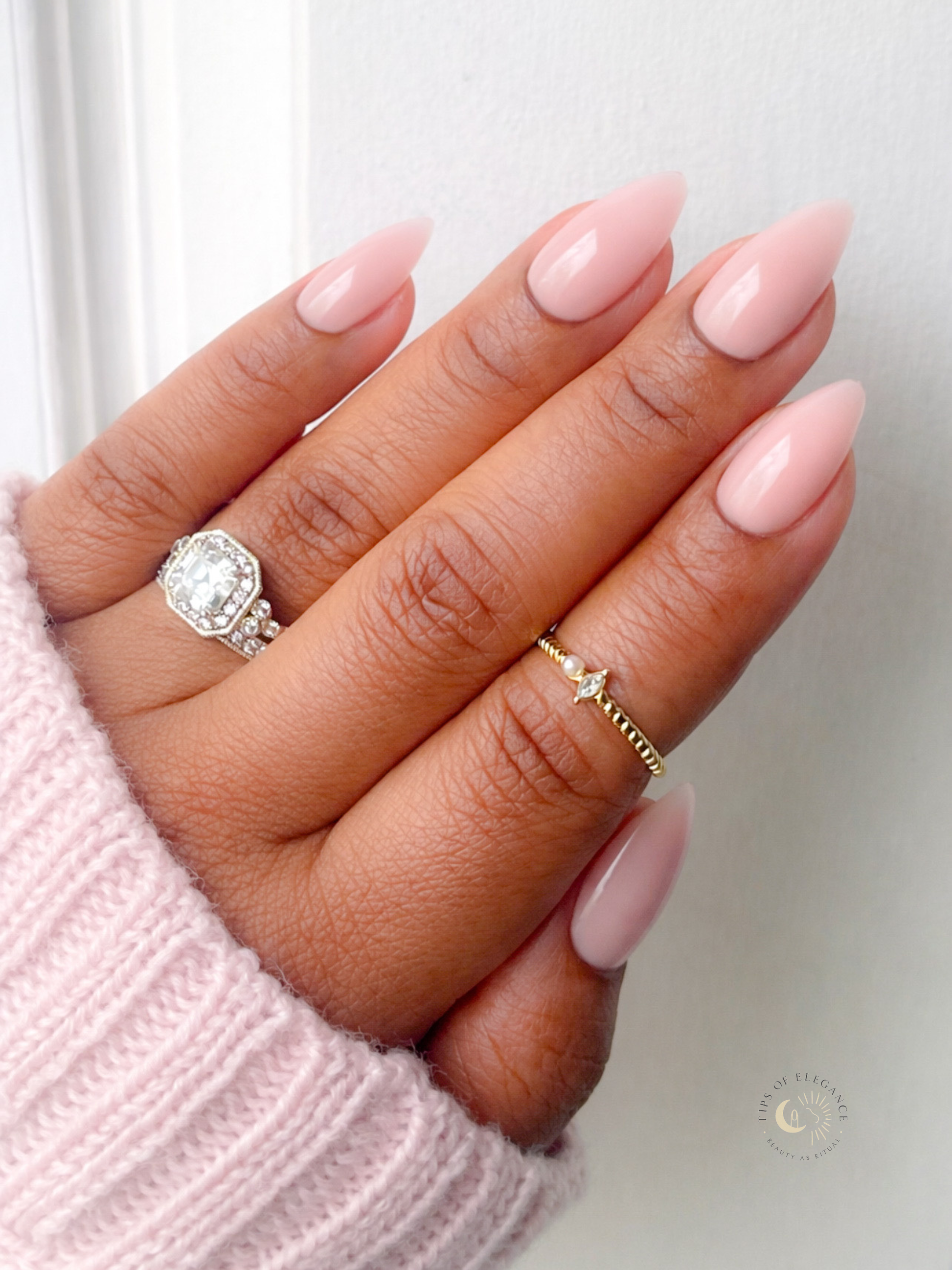 Hand with pink nail polish wearing two rings on a light background