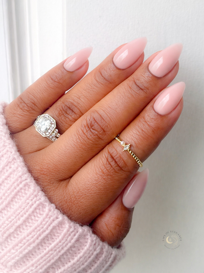 Hand with pink nail polish wearing two rings on a light background