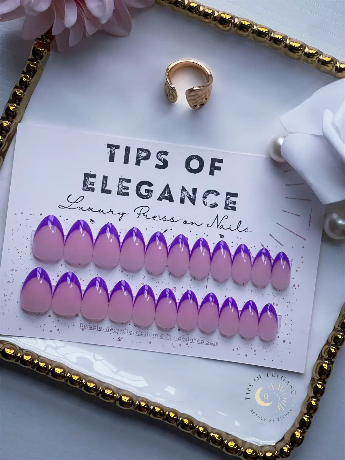 Purple and pink nail tips on a card labeled 'Tips of Elegance' with a ring and decorative elements.