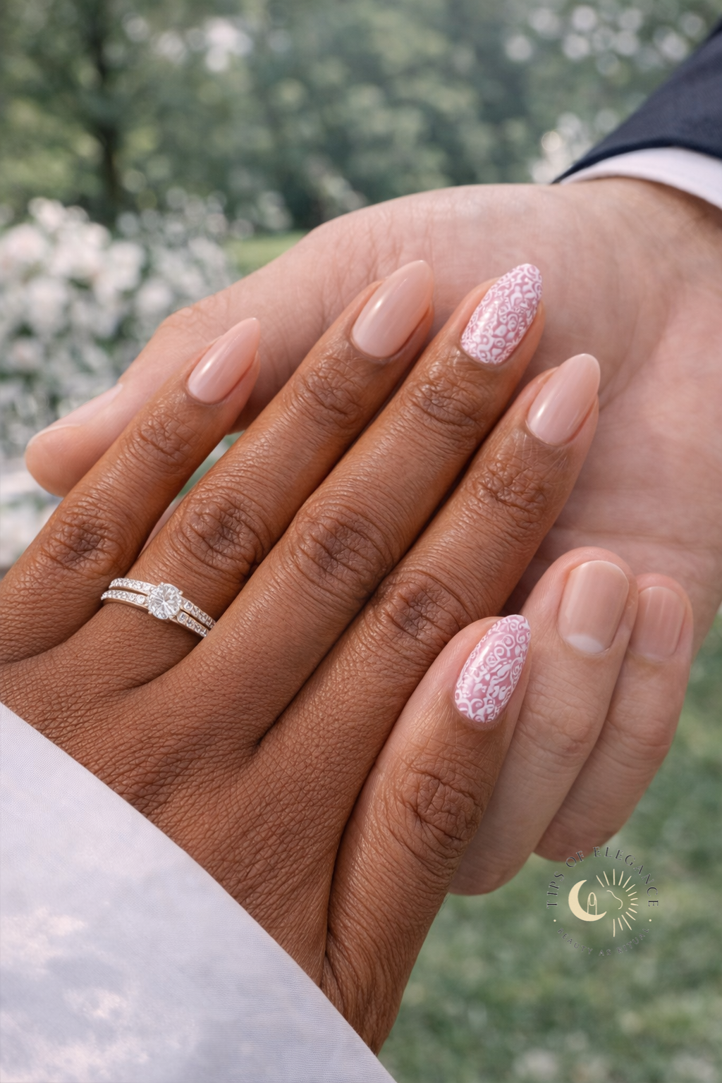 Two hands with wedding rings and milky nude almond polish  and white floral filigree scrolls lavender nail polish against a blurred natural background