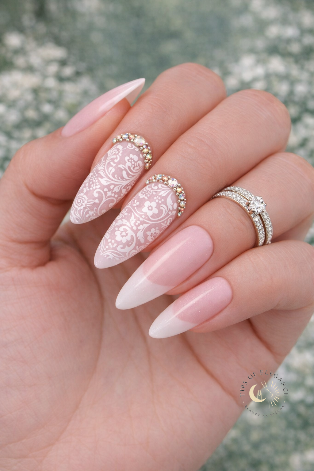Hand with filigree + pink and white nail design and a ring, against a blurred natural background