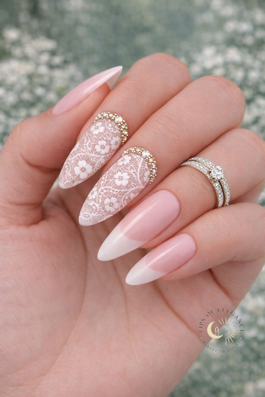 Hand with white lace and florals gold crystals+ pink and white French nail design on a blurred natural background