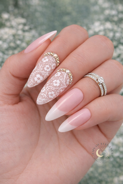 Hand with white lace and florals gold crystals+ pink and white French nail design on a blurred natural background
